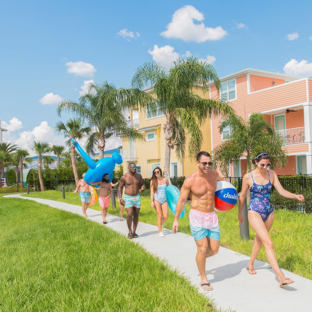 Group of friends carrying pool floaties walking along a sidewalk in the sunshine.