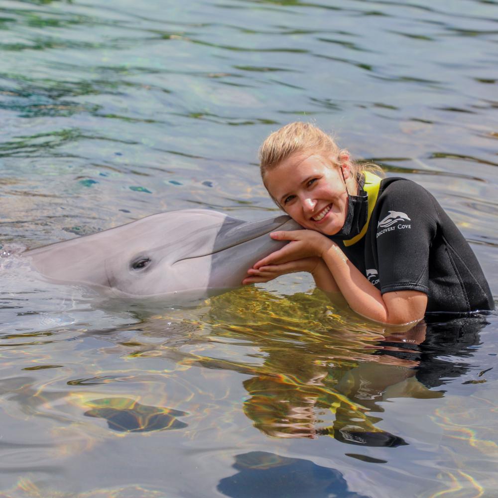 A smiling woman in a wetsuit gently hugs a dolphin while swimming in the clear waters at Discovery Cove in Orlando, Florida.