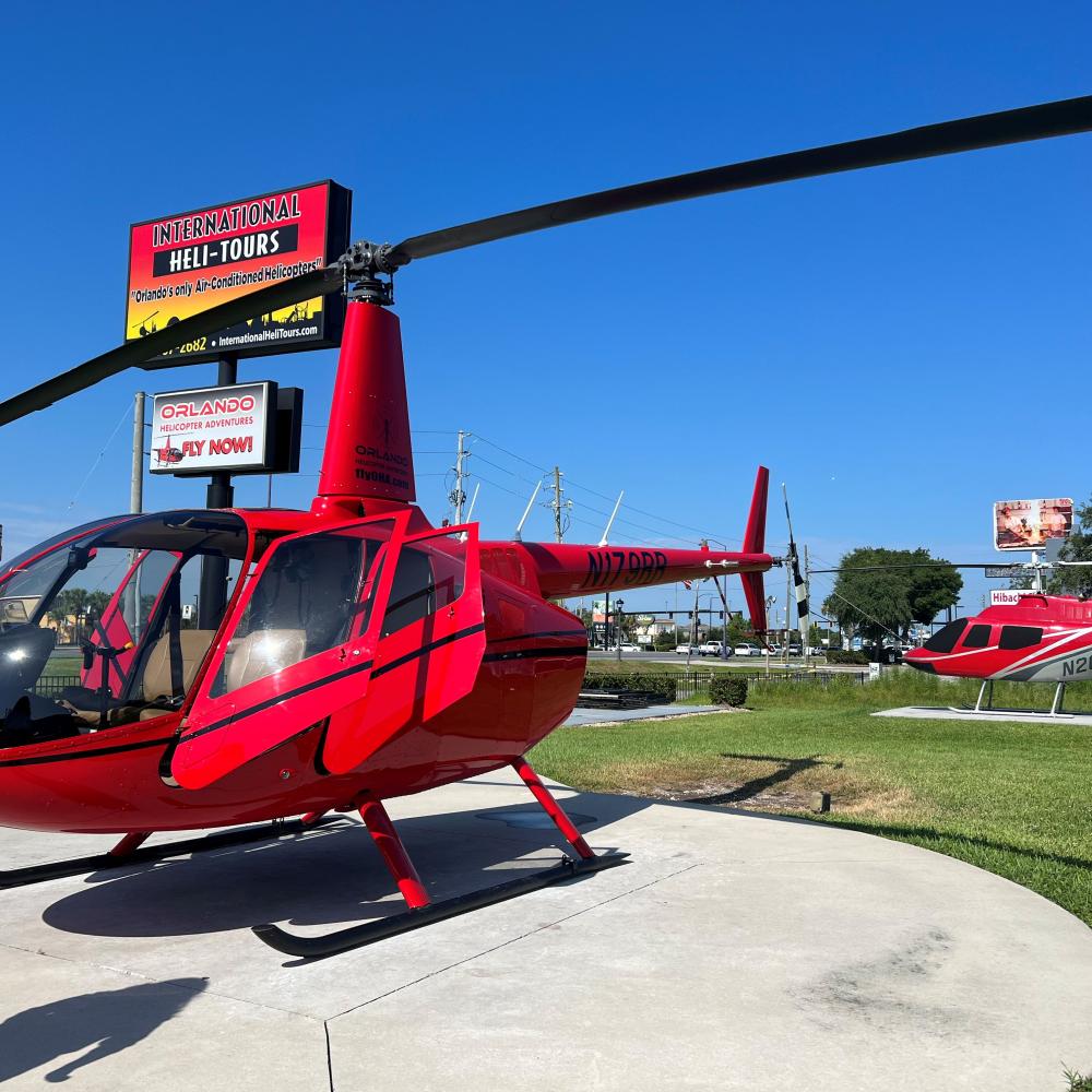 Two red helicopters parked on a sunny day at International Heli-Tours in Kissimmee, Florida, ready for scenic flights over Central Florida.
