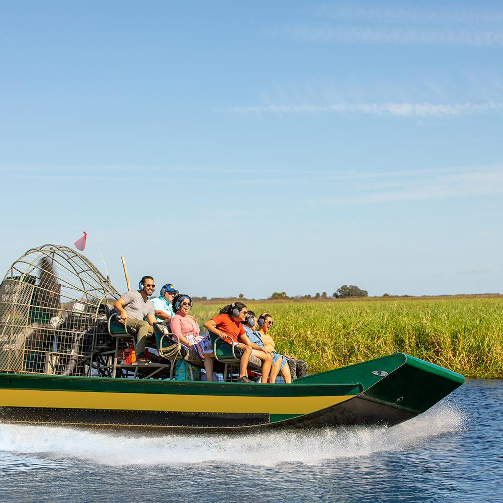 Group of people enjoying an airboat ride through the headwaters of the Everglades near Kissimmee, Florida, gliding over the water with lush green marshes under a clear blue sky.