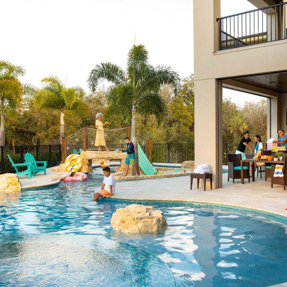 A multigenerational family enjoys time together at a Kissimmee vacation home, with kids playing in the private pool and adults preparing food on the outdoor patio.