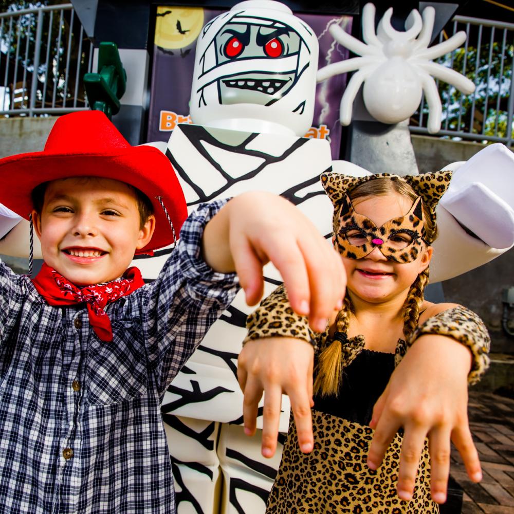 Two children dressed in Halloween costumes pose playfully with a LEGO® mummy character during Brick-or-Treat at LEGOLAND® Florida Resort.
