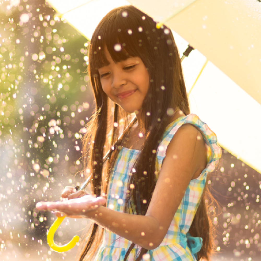 Smiling girl in a sun shower with an umbrella.