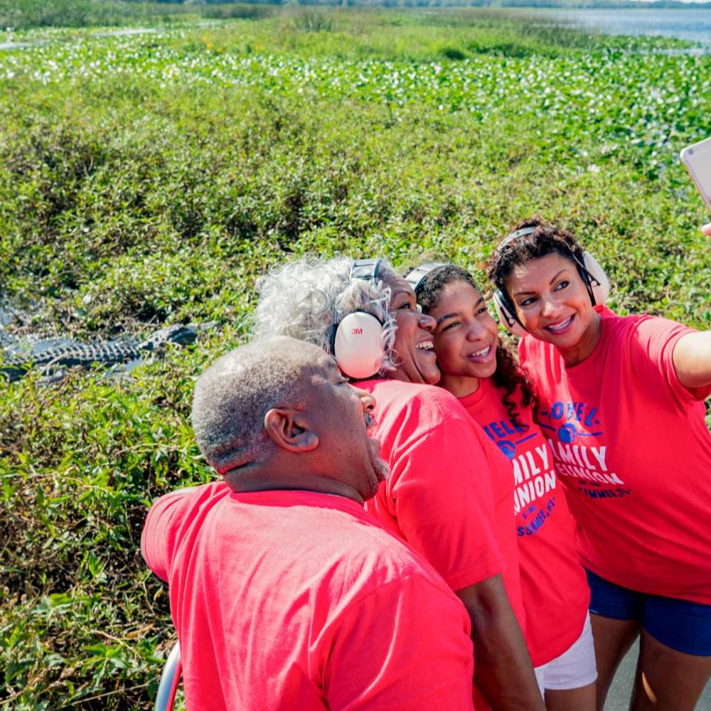 Family of four, wearing red shirts, taking a selfie with an aligator in the background