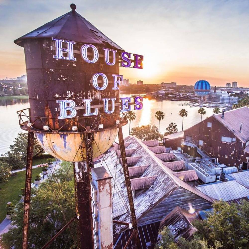 Sunset view of the House of Blues water tower and rustic concert hall at Disney Springs, with Lake Buena Vista, Florida, and surrounding attractions in the background.