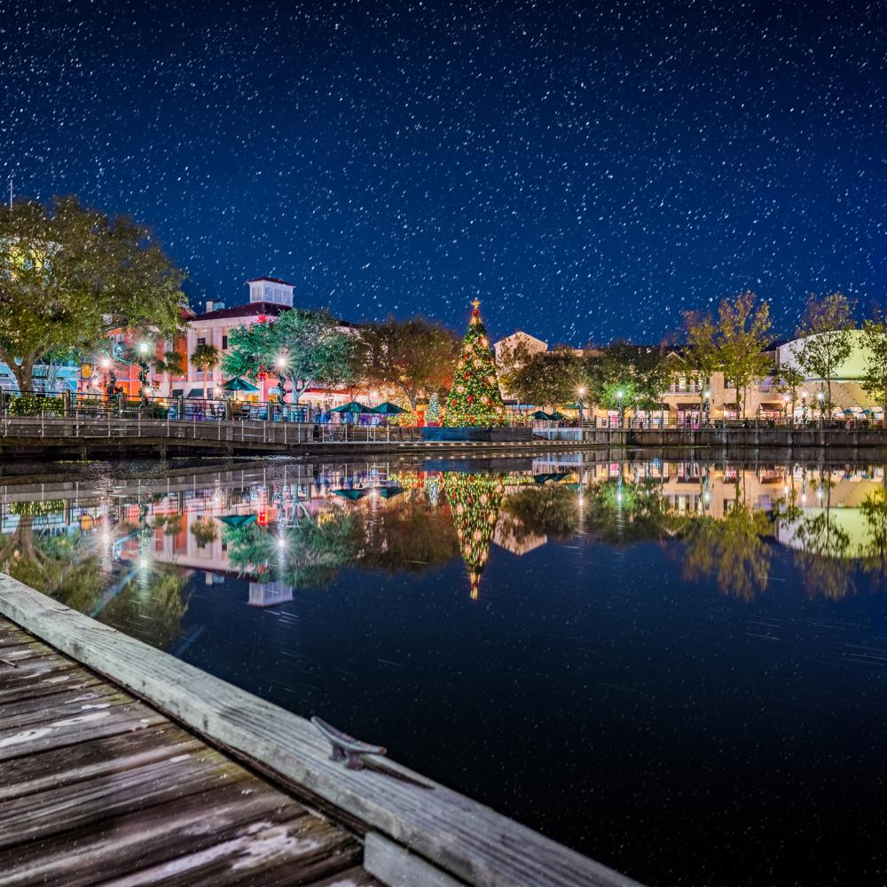 Fake snow falls on a festively-decorated Celebration Town Center at night.