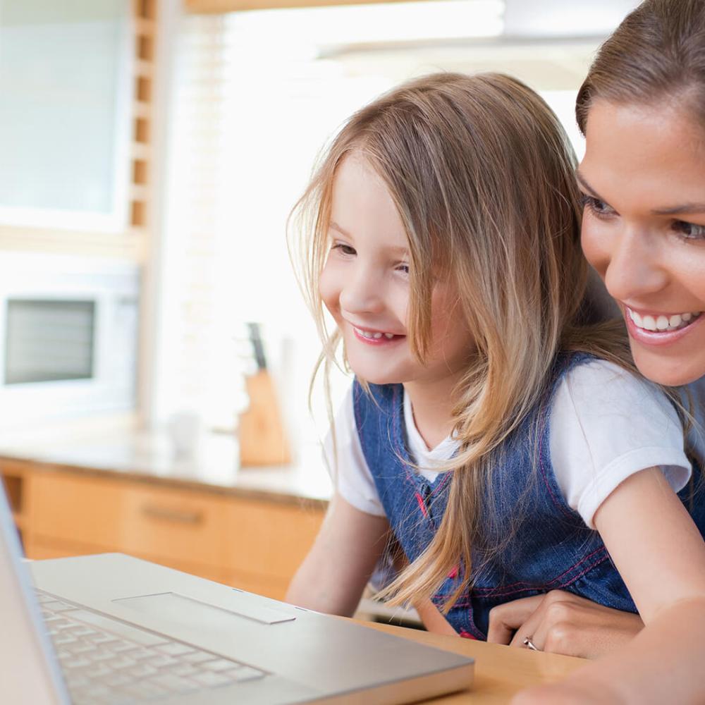 Mother and daughter smiling while planning their next family vacation on a laptop at home.