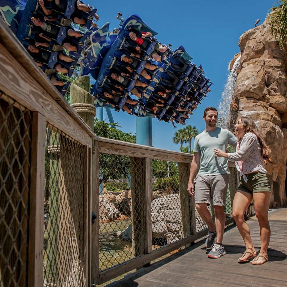 Couple at a theme park, walking on bridge with roller coaster in background
