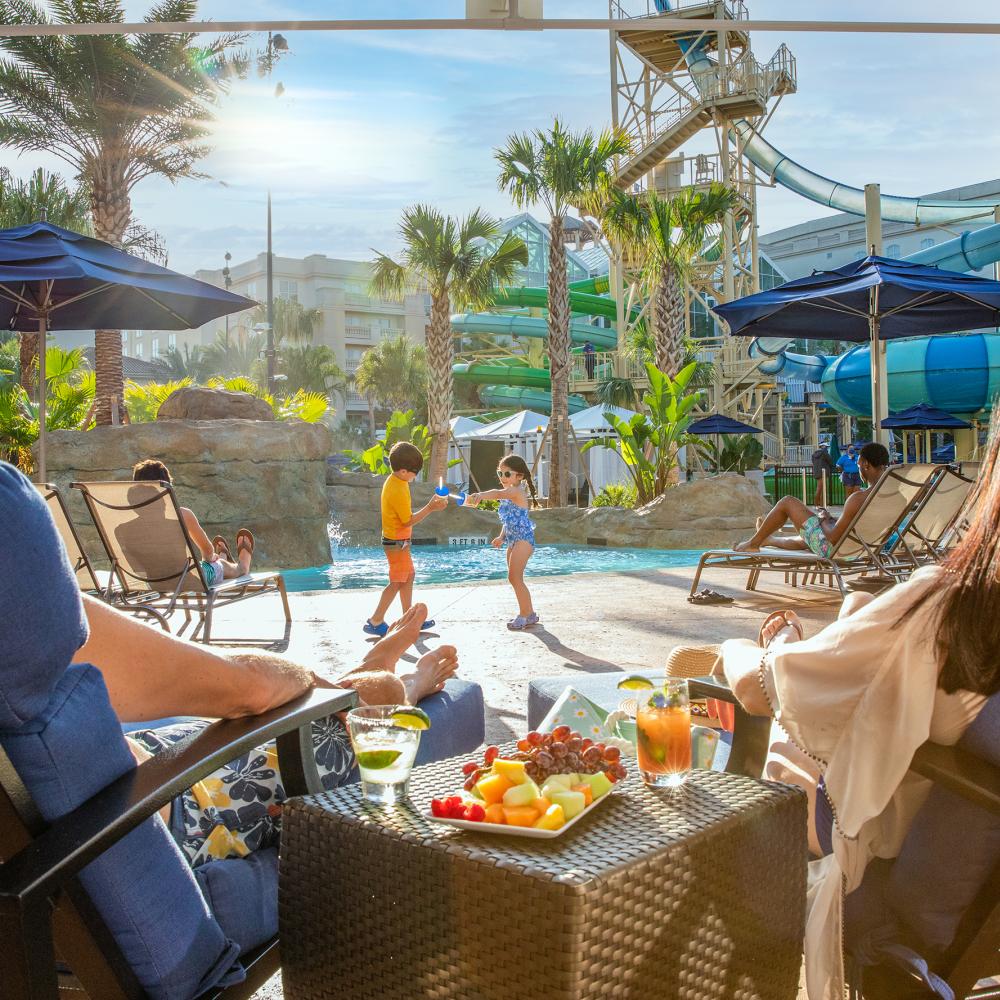 Two people lounging by the pool at the Gaylord Palms Resort and Convention Center enjoying drinks and food. 
