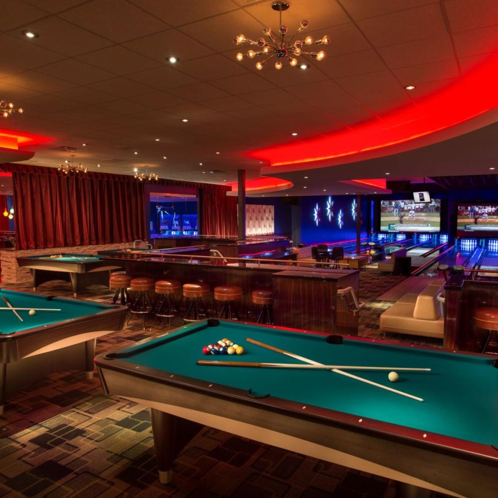 A stylish entertainment venue with pool tables, a bowling alley, and large-screen TVs glowing under red and blue lights in Kissimmee, Florida.