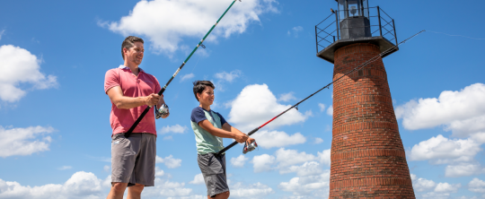 A father and son fishing together near a brick lighthouse on a sunny day in Kissimmee, Florida.