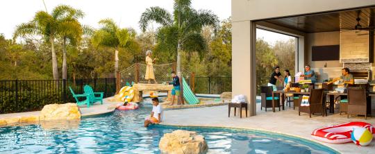 A multigenerational family enjoys time together at a Kissimmee vacation home, with kids playing in the private pool and adults preparing food on the outdoor patio.