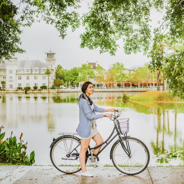 Woman smiling while standing beside her bicycle along a scenic lakeside path in Celebration, Florida.