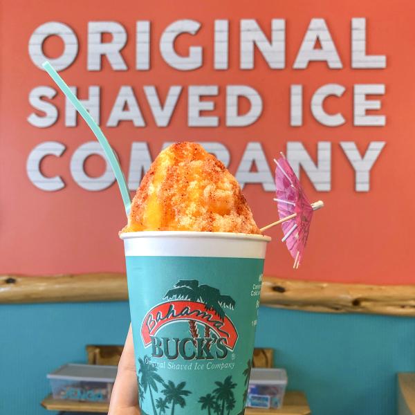 person holding up a cup of orange flavored shaved ice from Bahama Bucks