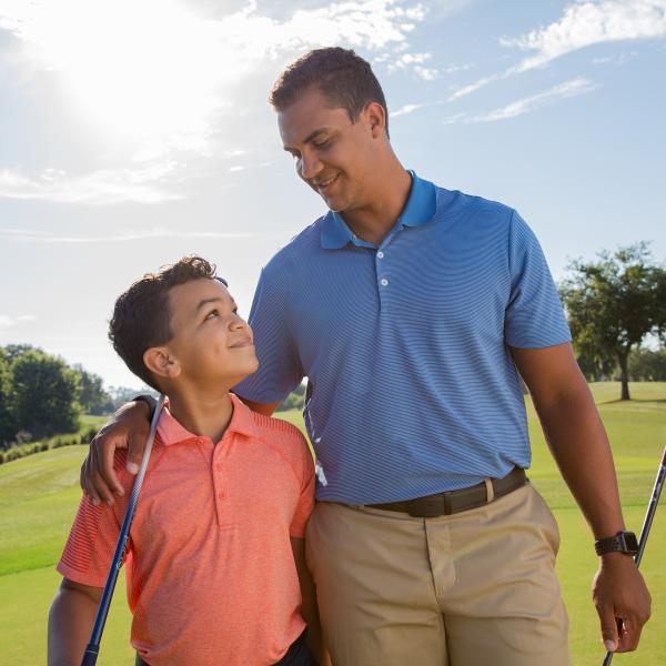 Young boy walking with dad with arm around him on the golf course