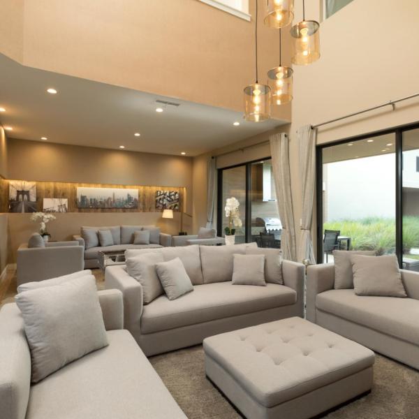 Spacious, modern living room with plush sectional seating, high ceilings, pendant lighting, and sliding glass doors opening to a private patio.