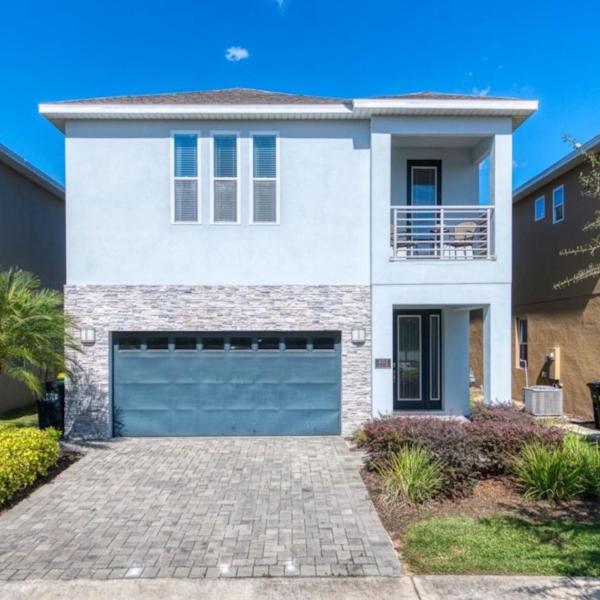 Modern two-story vacation home in Kissimmee with a private driveway, balcony, landscaped yard, and contemporary exterior design under a clear blue sky.