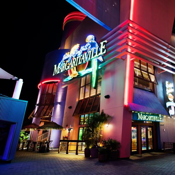 Jimmy Buffett’s Margaritaville at Universal CityWalk glows at night, with colorful neon signs, palm accents, and outdoor seating lighting up the walkway.
