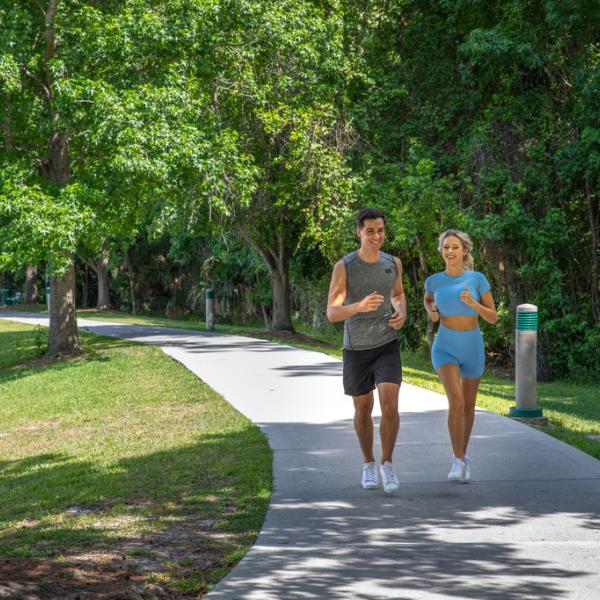 Man and woman jog on a walking path surrounded by trees. 