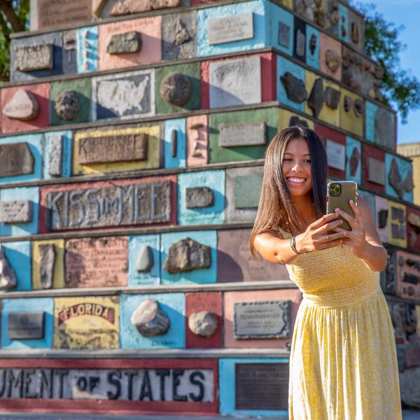 Girl in yellow dress takes photo in front of Monument of States in Downtown Kissimmee.