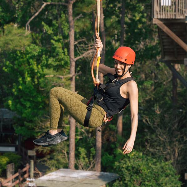 A woman wearing a safety harness and helmet smiles while ziplining through the treetops at Gatorland in Kissimmee, Florida.