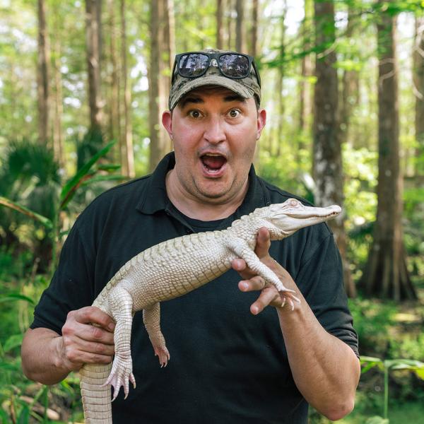 Jeff Musial holds an albino alligator in front of the trees at Wild Florida.