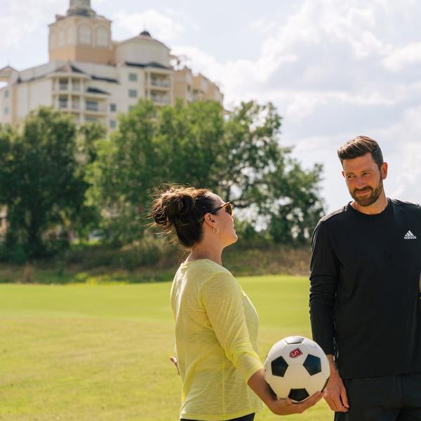 Luke Boden and Jen Bonner hold soccer balls on the footgolf course in front of Reunion Resort