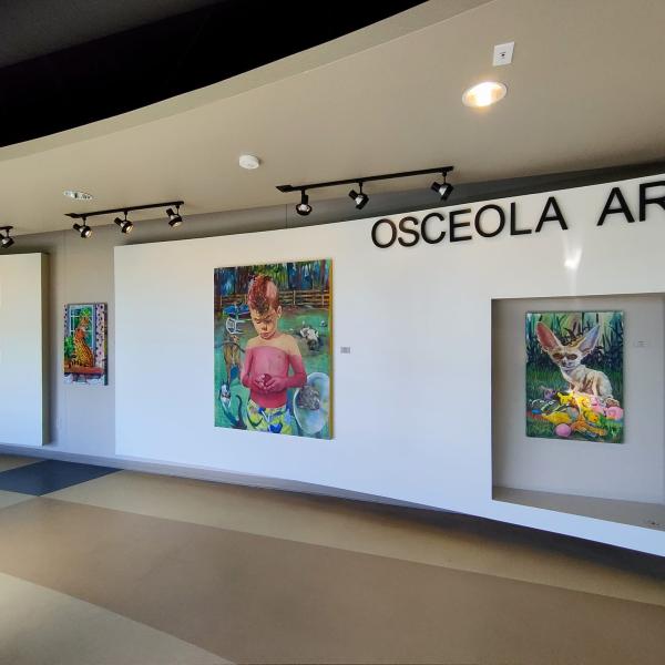 Interior view of the Osceola Arts gallery showcasing colorful paintings displayed under spotlights, including portraits and animal-themed artwork.