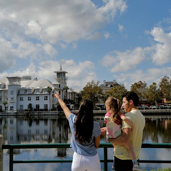 A family stands by the lake in Celebration, Florida, admiring the charming pastel-colored buildings and waterfront views on a sunny day.