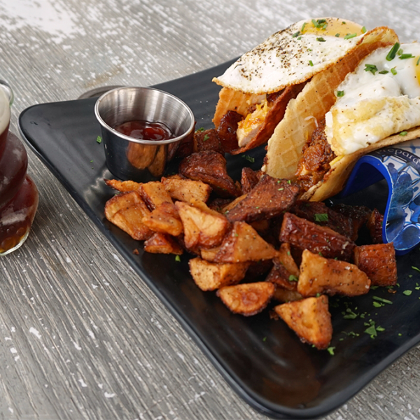Plated meal of egg tacos and potato wedges on a black plate at Loading...Gastrobrunch.