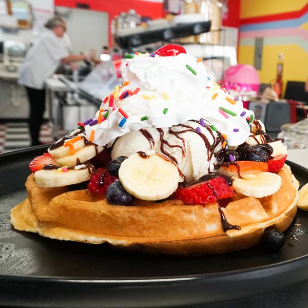 Stack of waffles with bananas and strawberries topped with whip cream at Pops Waffle & Ice Cream Shoppe in Downtown St. Cloud