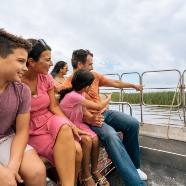 A family enjoys an airboat ride through the wetlands at Wild Florida, smiling and pointing at wildlife in the distance.