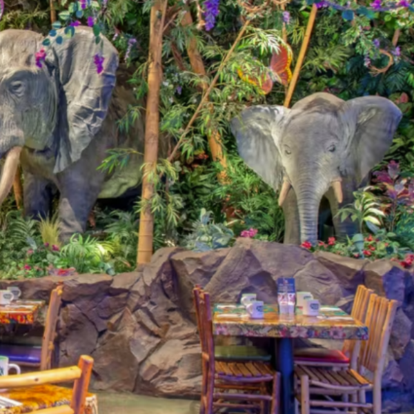 Dining tables surrounded by lush greenery and life-sized elephant sculptures in a jungle-themed restaurant setting.