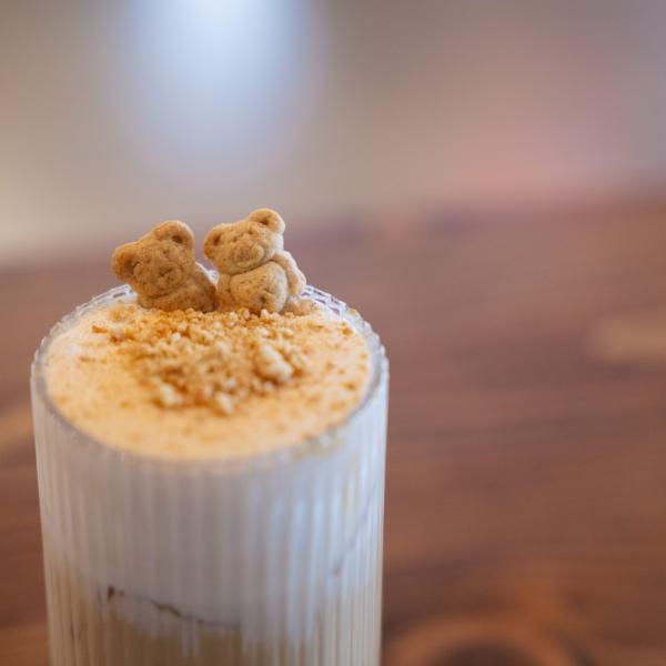Two light brown graham bears sit side-by-side on a foamy top of an iced coffee drink.