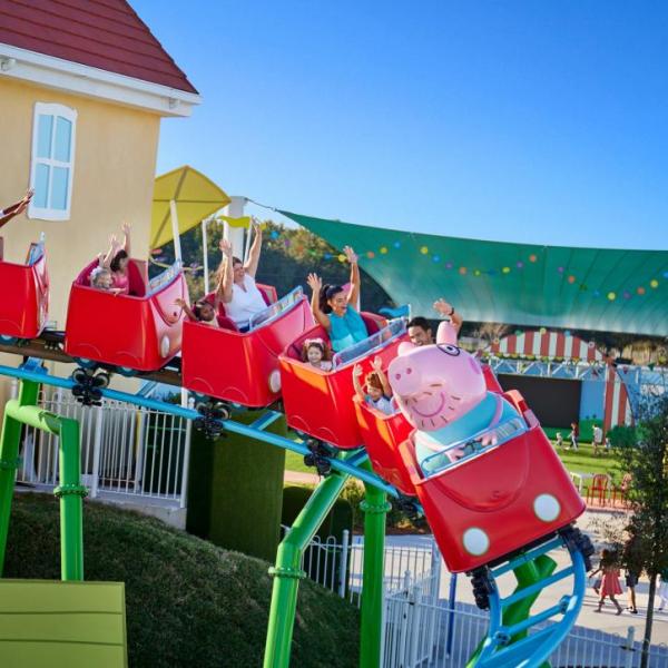 Families with young children ride Daddy Pig’s Roller Coaster at Peppa Pig Theme Park near LEGOLAND® Florida, smiling and raising their hands in excitement.