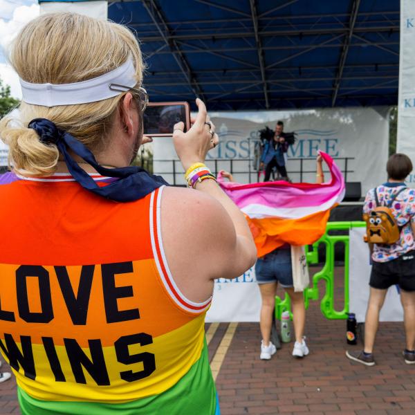 A person wearing a ‘LOVE WINS’ shirt taking a photo of the stage performance at the PrideFest Kissimmee event.