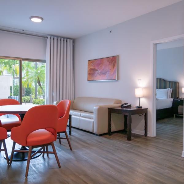 A view of the wellness suites shows a dining set that seats four, a couch, sliding glass door that lets in lots of natural light, a kitchenette, and spacious bedrooms.