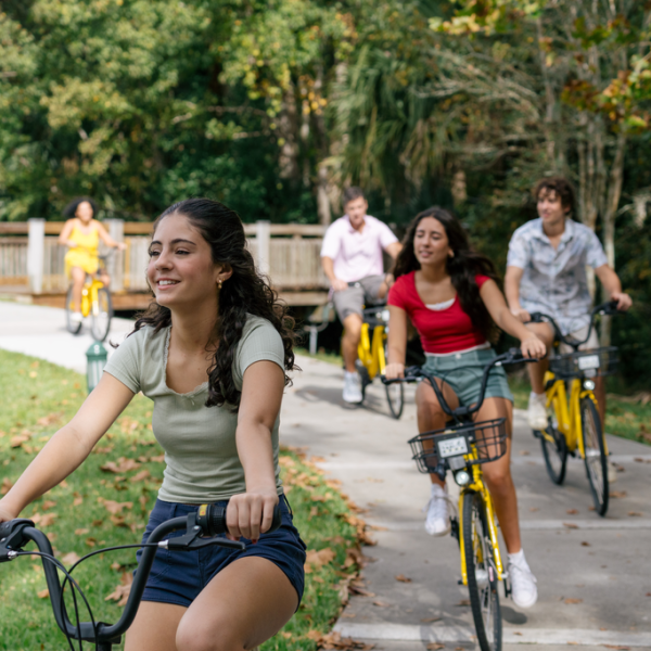 A group of friends rides yellow bikes along a paved trail surrounded by trees and greenery in Kissimmee, Florida.