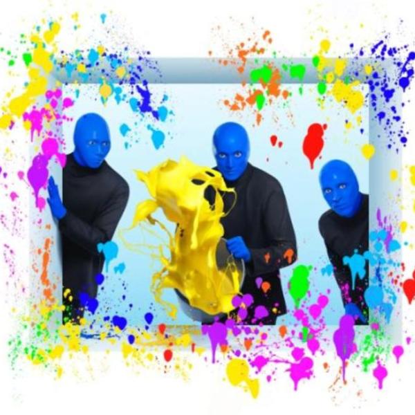 Three performers from Blue Man Group stand against a light background, holding and splashing vibrant yellow paint, surrounded by colorful paint splatters.