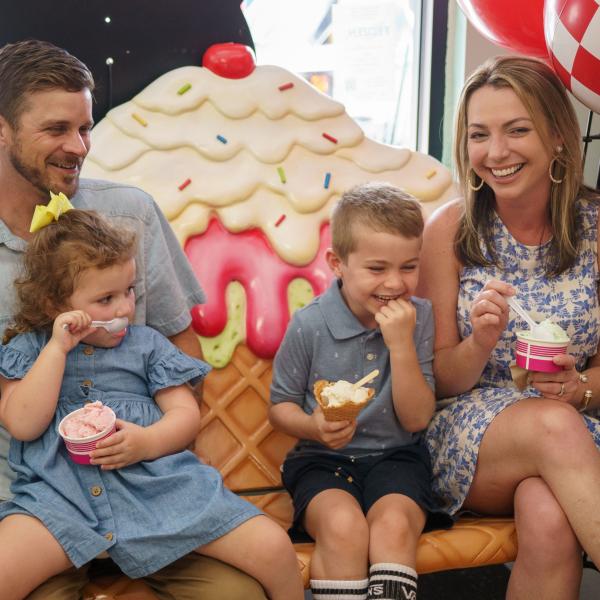A smiling family enjoys ice cream together while sitting on a whimsical, oversized ice cream-themed bench inside Pops Waffle & Ice Cream Shoppe in Downtown St. Cloud, Florida.