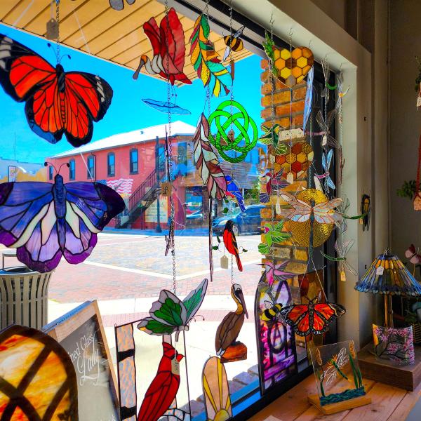 Colorful stained glass artwork, including butterflies and dragonflies, hanging in a sunny window at The Stained Glass Lady in Downtown St. Cloud, Florida.