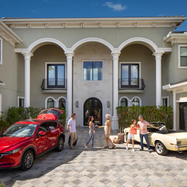 Family greeting each other in the driveway of a luxury vacation home in Kissimmee, Florida, with cars parked and luggage ready for a getaway.