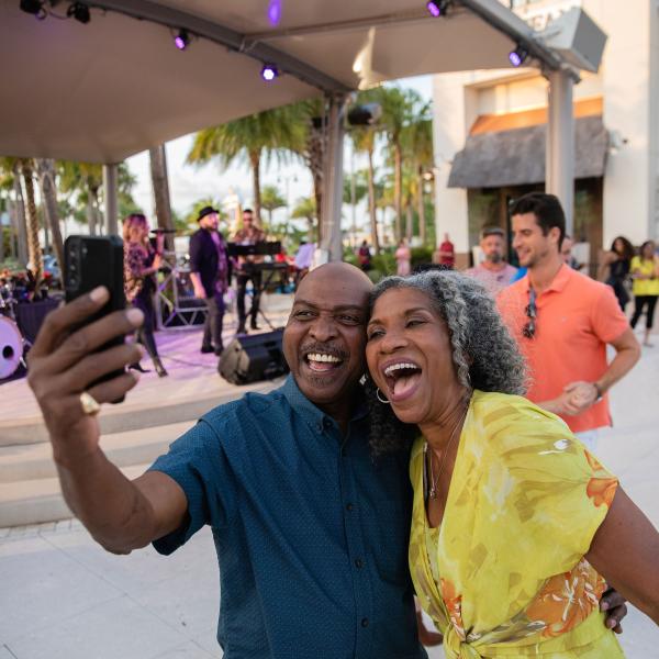 Couple taking a selfie in front of a live band at Promenade at Sunset Walk in Kissimmee, Florida.