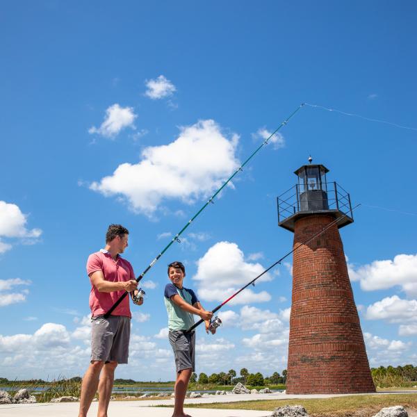 A father and son fishing together near a brick lighthouse on a sunny day in Kissimmee, Florida.