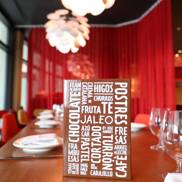 Close-up of a dessert menu at Jaleo by José Andrés, displayed on a wooden dining table set with plates and glasses in a warm, modern restaurant interior with red accents.