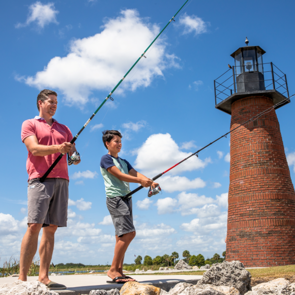 A father and son fishing together near a brick lighthouse on a sunny day in Kissimmee, Florida.
