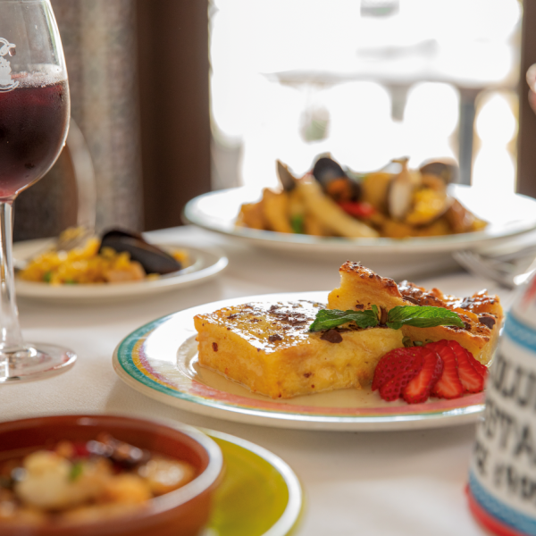 Close-up of a dessert plate with bread pudding and strawberries at Columbia Restaurant, with sangria and seafood dishes softly blurred in the background.