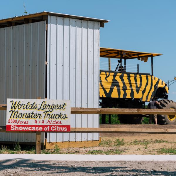 Sign for “World’s Largest Monster Trucks” and 4x4 rides at Showcase of Citrus with a large striped monster truck in the background.