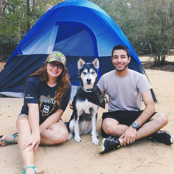A man, woman, and dog pose outside their tent