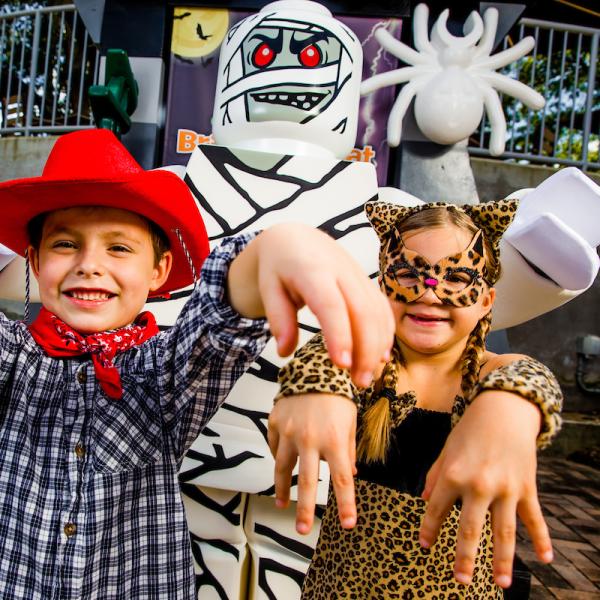 Two children dressed in Halloween costumes pose playfully with a LEGO® mummy character during Brick-or-Treat at LEGOLAND® Florida Resort.